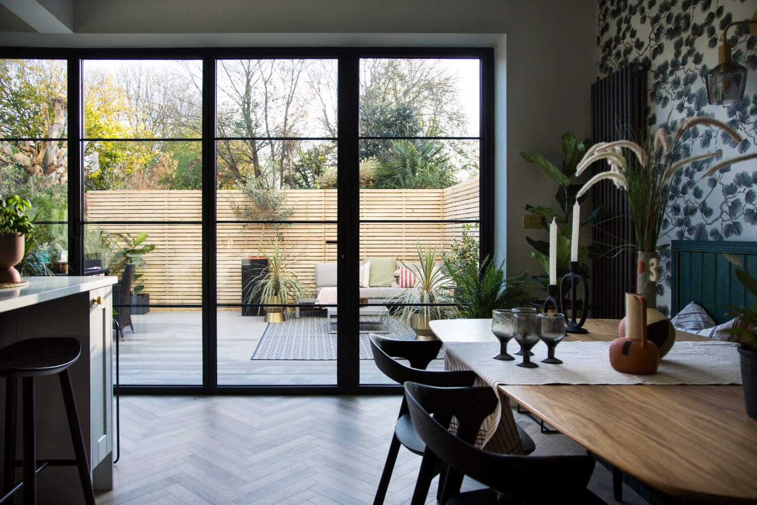 Dark shaker-style kitchen island with bar stools, doors opening onto a herringbone-floored dining area